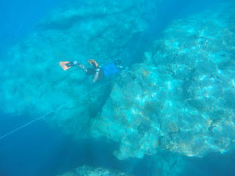 Underwater, a man wearing a snorkel, fins, and mask swims down to a coral reef with an instrument tied to a tether.