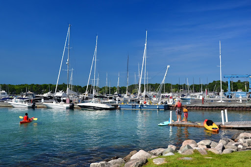 A marina full of boats. People stand on a pier near a person in a kayak in the water.