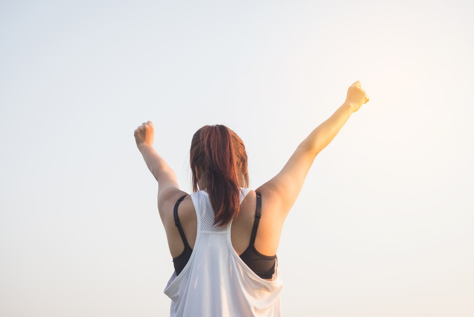 a woman and workout clothes throws both rms triumphantly into the sky