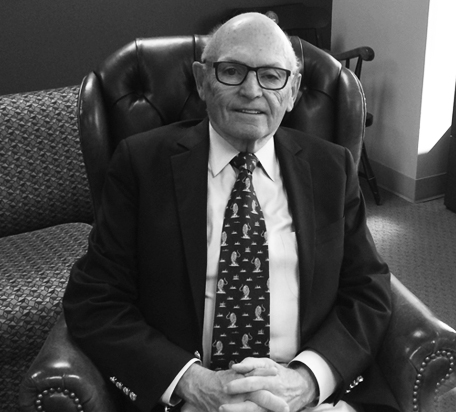 Dr Dunner, an older gentleman with glasses sitting in an armchair wearing a suit and tie, completed a review of TMS therapy as a depression treatment in his study for the university of washington.