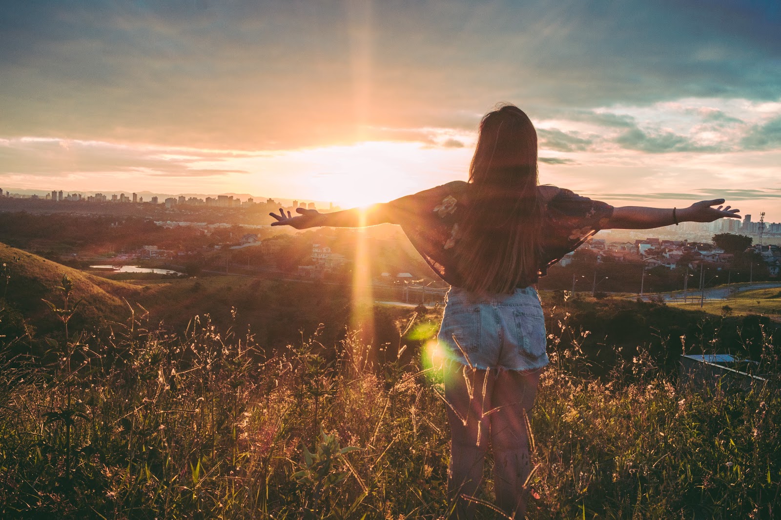Woman standing in a field with her arms open to the sun