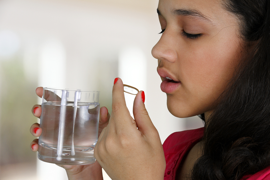 Adolescent girl takes pill with water.