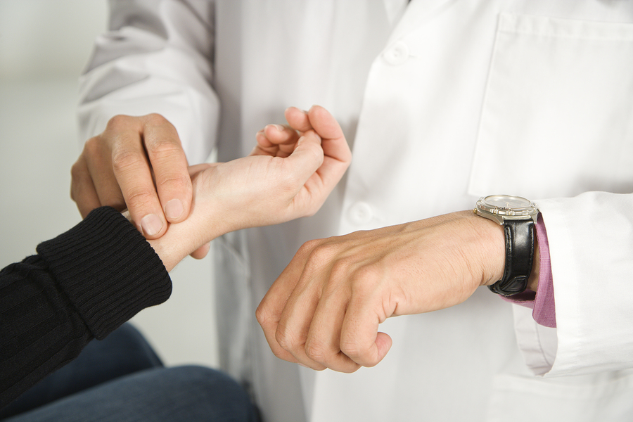 Physician checks patient's heart rate using watch and pulse from wrist.