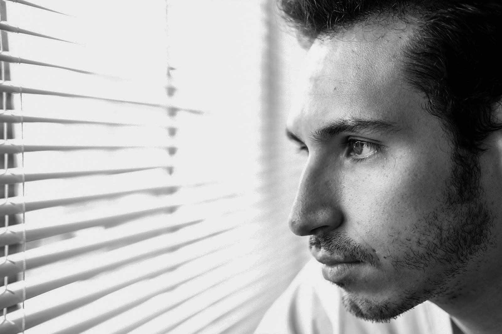Man stares through blinds and out the window