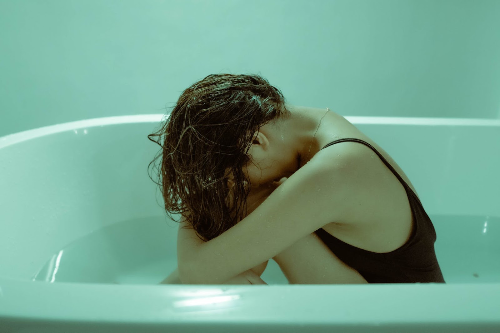 Depressed girl cries in blue bathtub