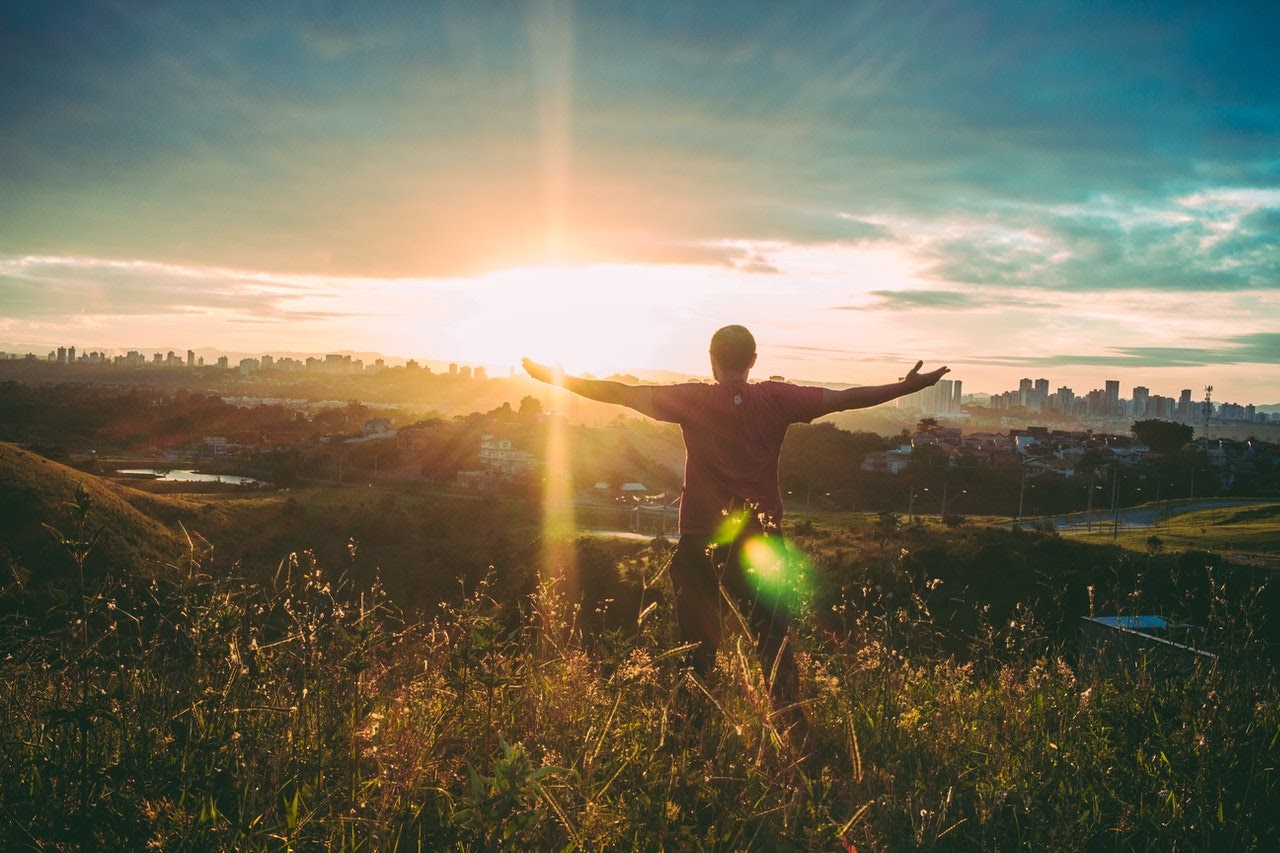 A man stands on top of a hill with his arms spread out, appearing to be feeling euphoric and in a positive mood.