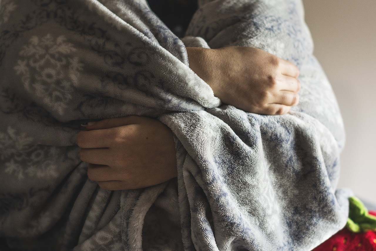 A person wraps up in a blanket appearing to be cold, another physical symptom of anxiety
