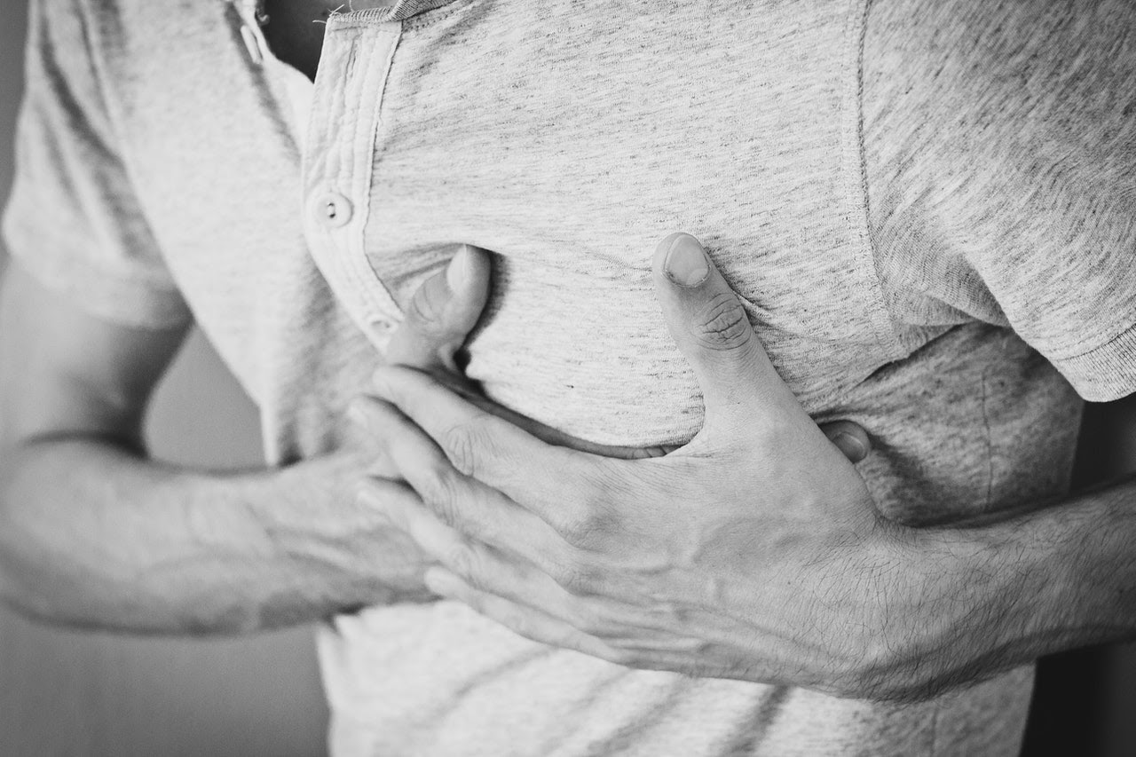 A man holds over his heart as if it is racing, a common physical symptom of anxiety.