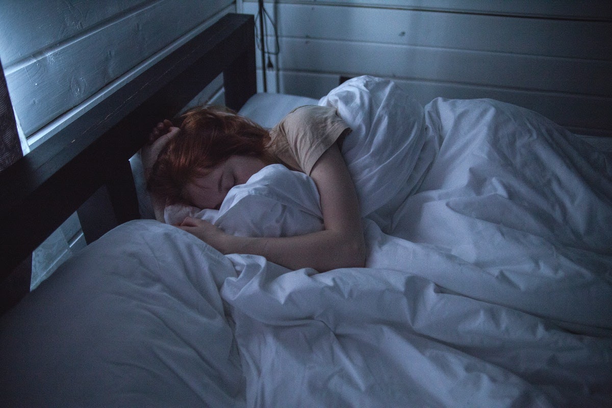 A woman is in bed appearing to be extremely fatigued, which is one of the physical symptoms that grief can cause.