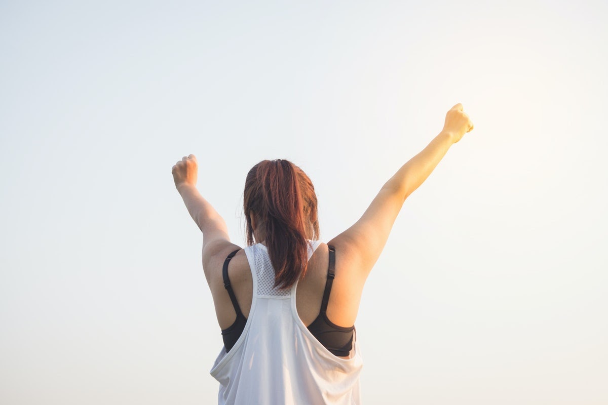 A woman stands with her arms in the air in an empowered pose.