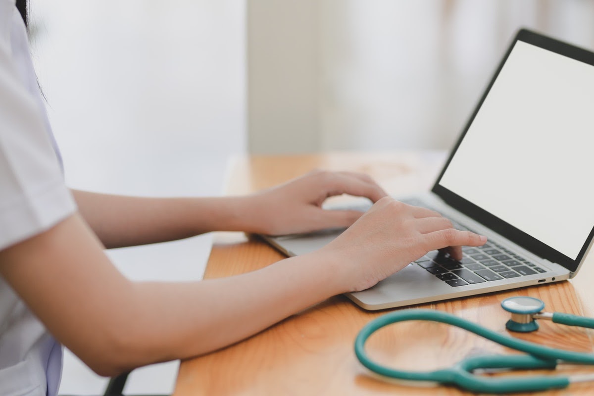 A healthcare worker sits at a laptop to utilize telehealth technology.