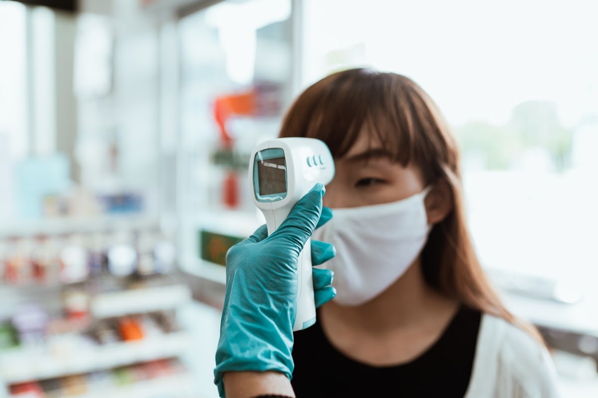 A woman gets her temperature taken as part of a screening procedure within a business.