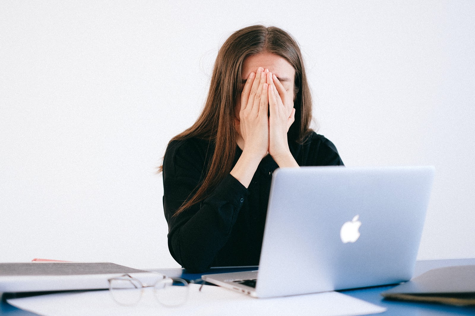 A woman sits with her laptop looking extremely upset and stressed, possibly from an event such as job loss.