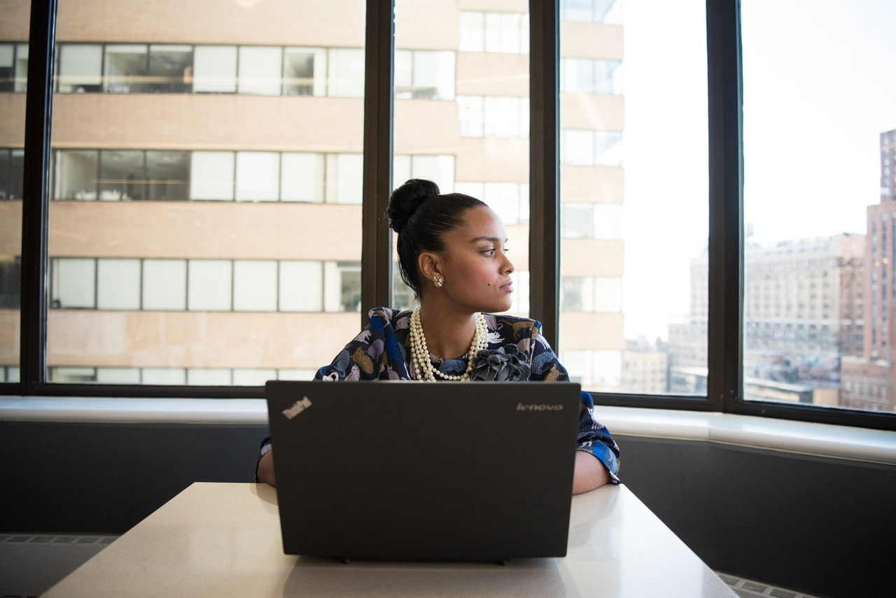 Girl works at a laptop in an office and stares off in the distance away from her computer screen.