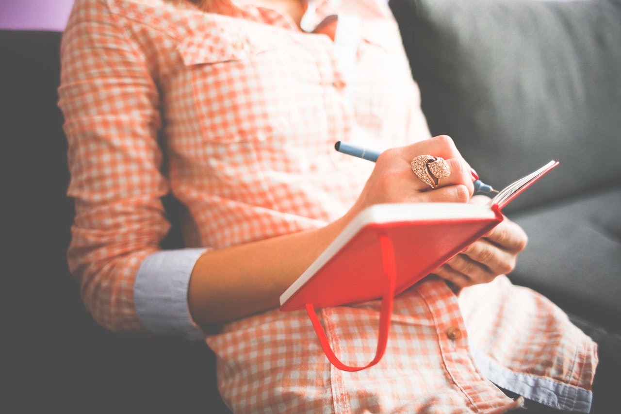 Person in a button down shirt writes in a bright orange journal.