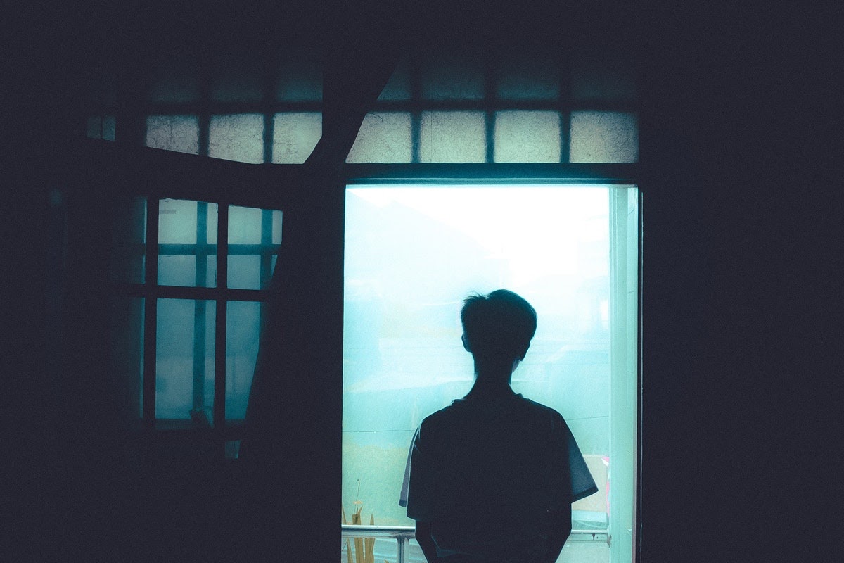 man looking out the window with lights off