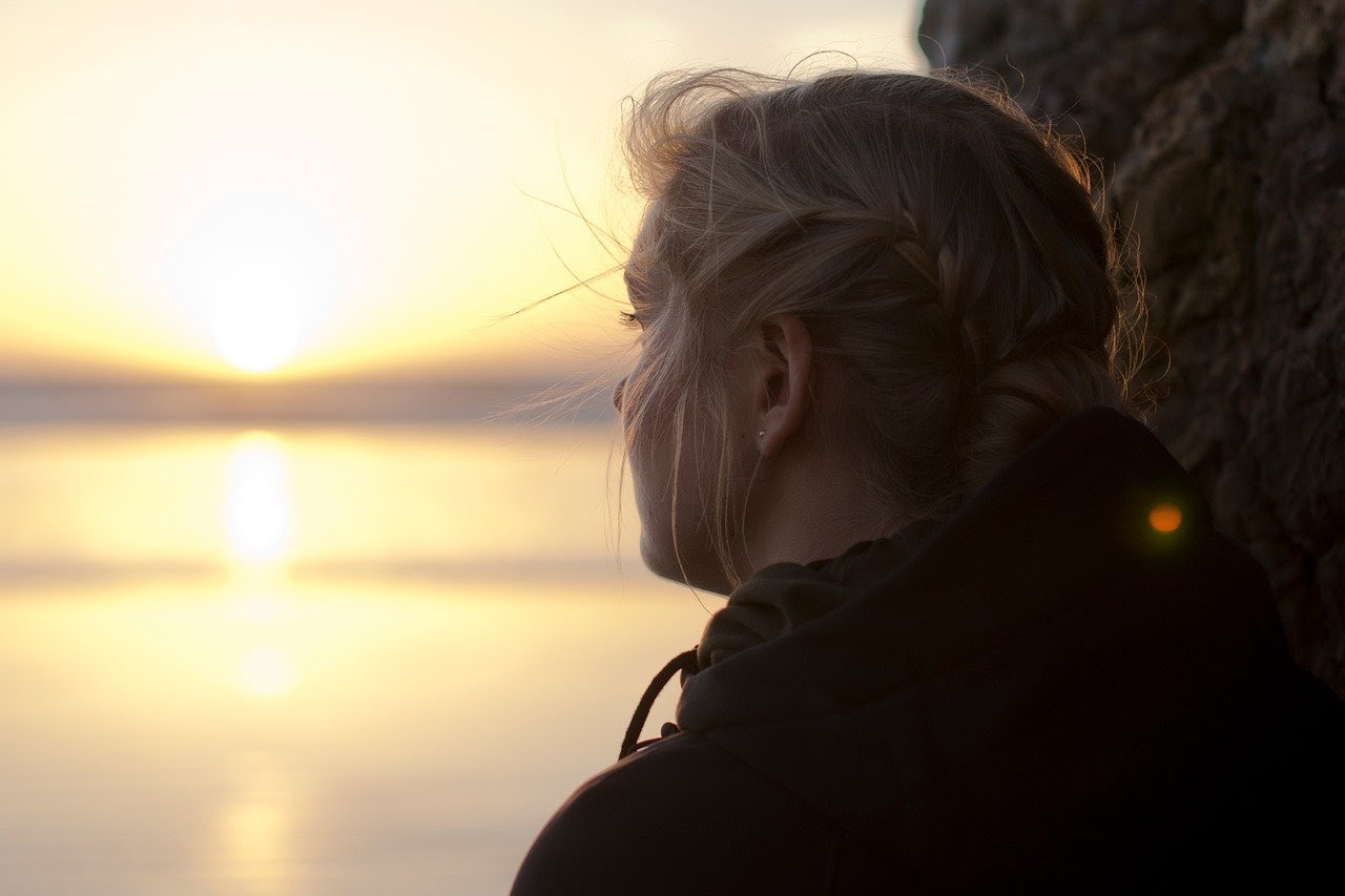 Girl looks depressed while staring out at a sunset.