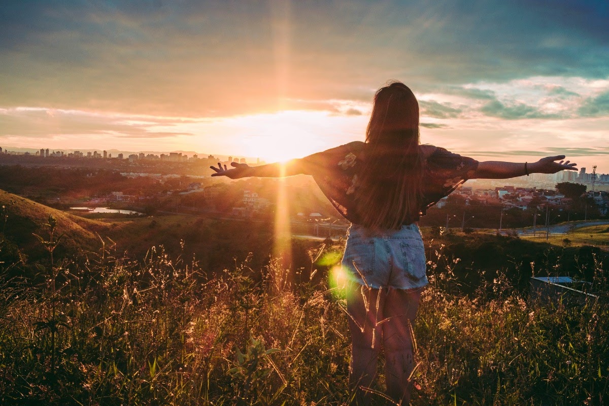 woman with arms out in front of sunset