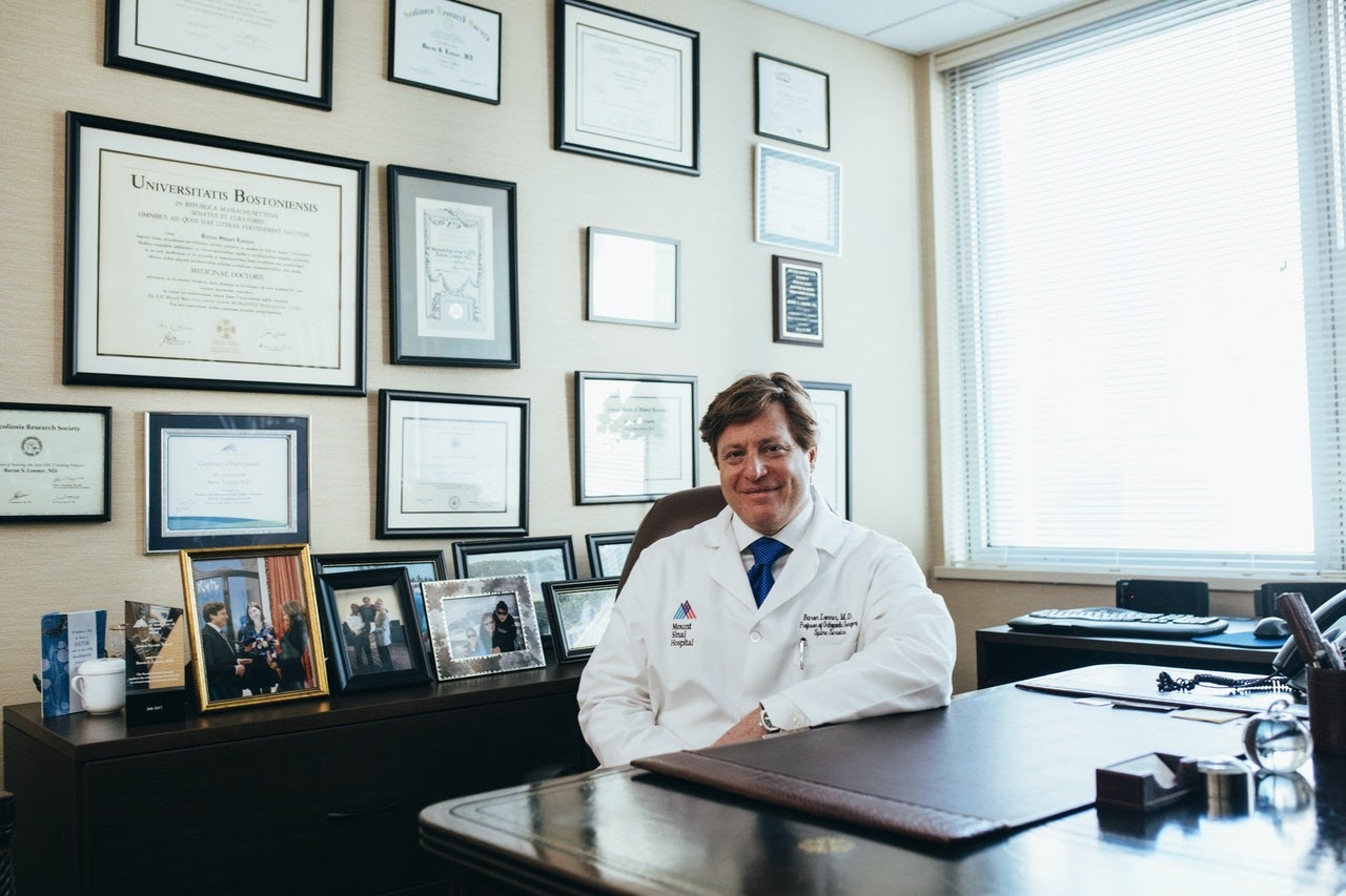 Doctor in white jacket smiles while sitting in his office