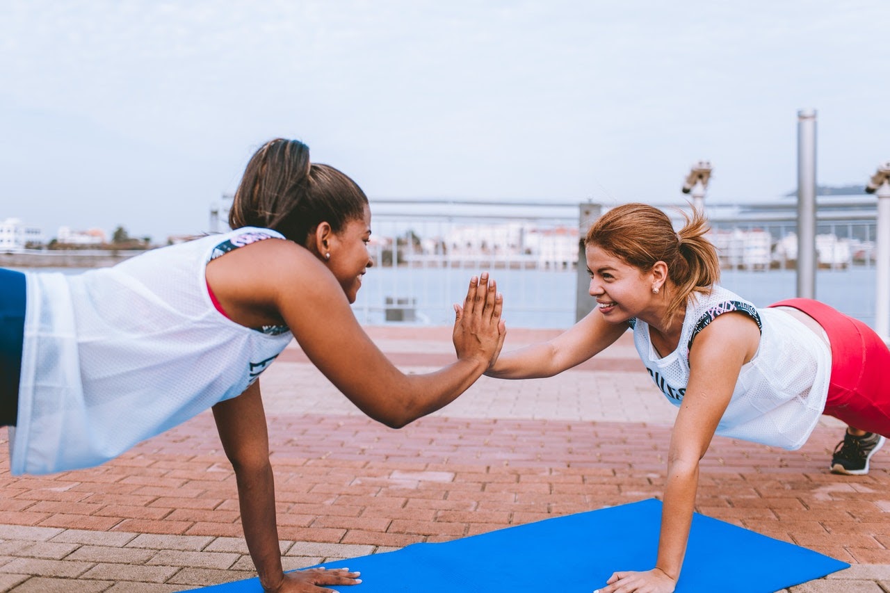 Two young women stretch will doing yoga together and smile