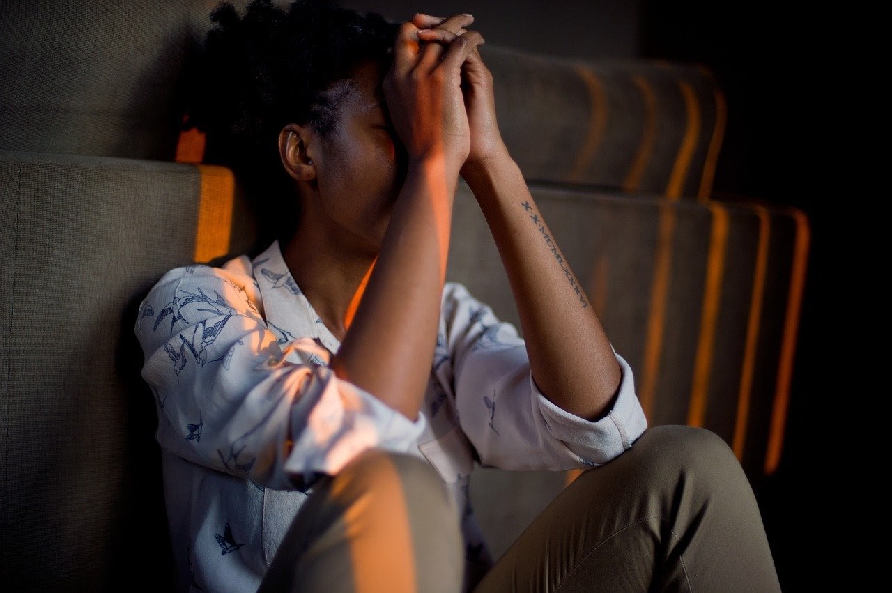 Young woman sits with arms propped up against her face in distress and stress