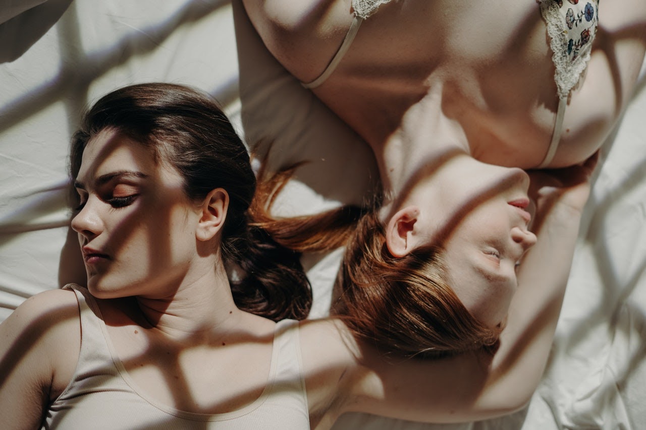Two women sleep next to each other on a bed, facing away from each other