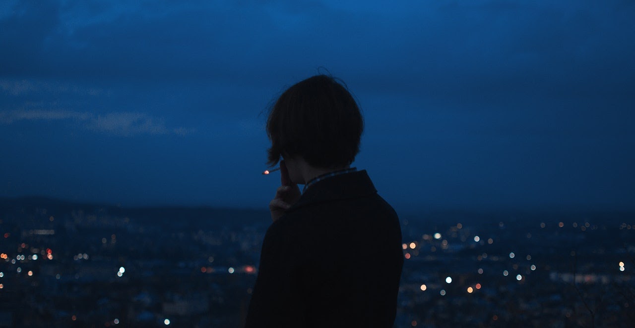 Man smokes a cigarette while looking over a city late in the evening