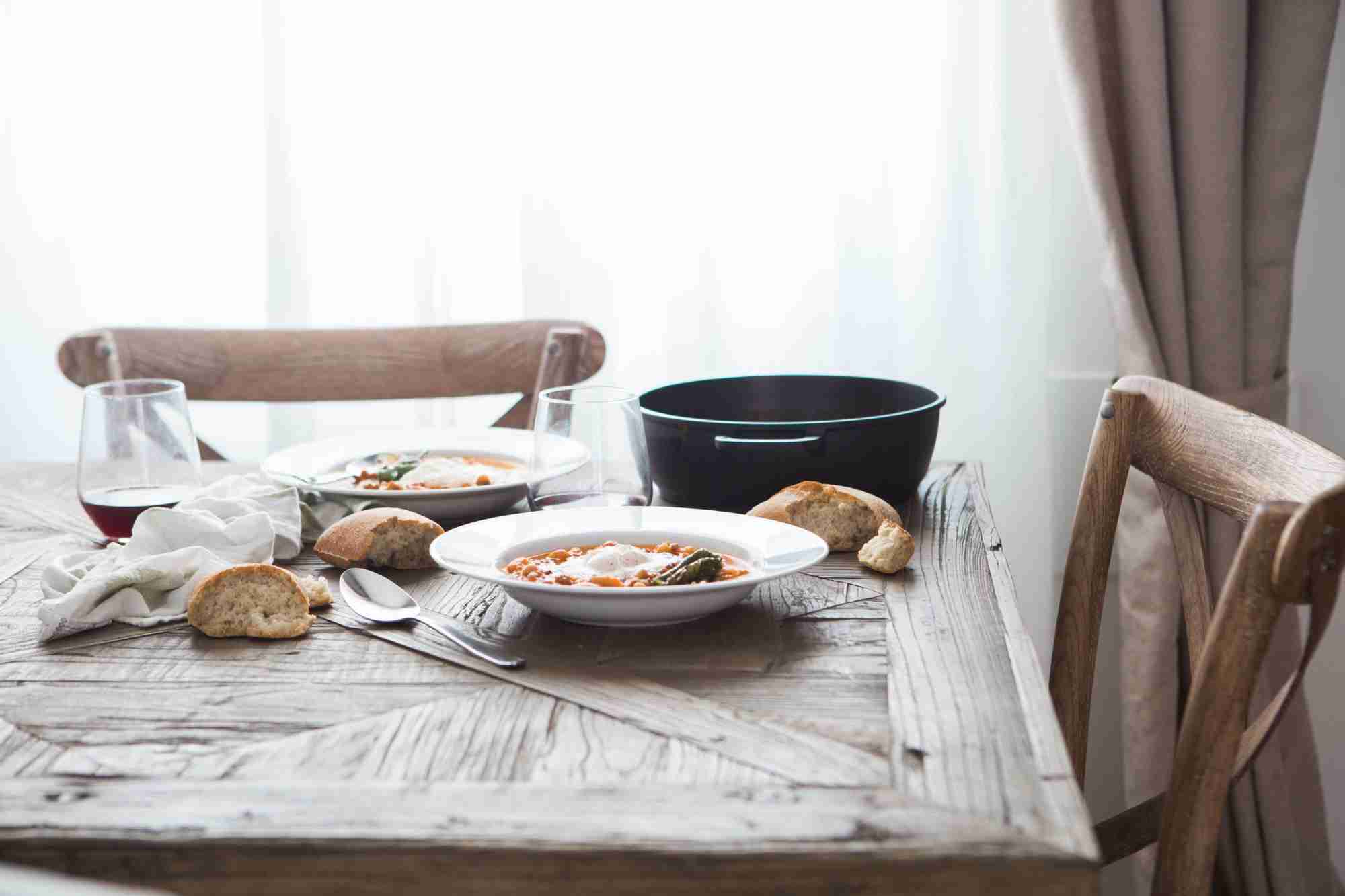 Dos platos de puchero y un par de vasos de vino encima de una mesa de madera.