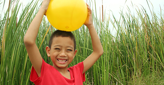 smiling boy holding yellow ball over his head