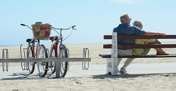 senior man and woman on bench next to bikes at beach