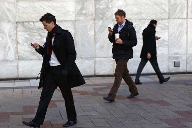 men in suits walking while looking down at phone
