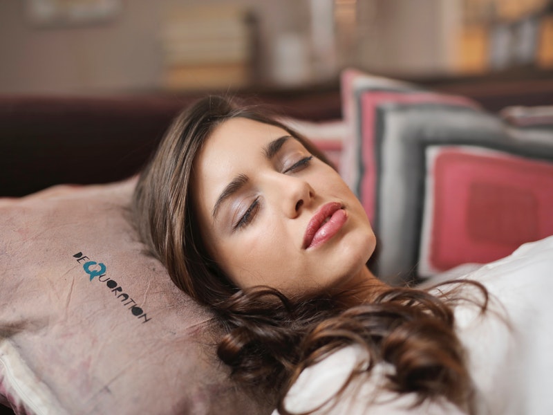 A woman rests with her head elevated on several pillows.