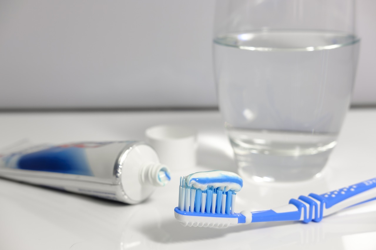 A toothbrush with toothpaste, a tube of toothpaste, and a glass of water sit on a countertop.