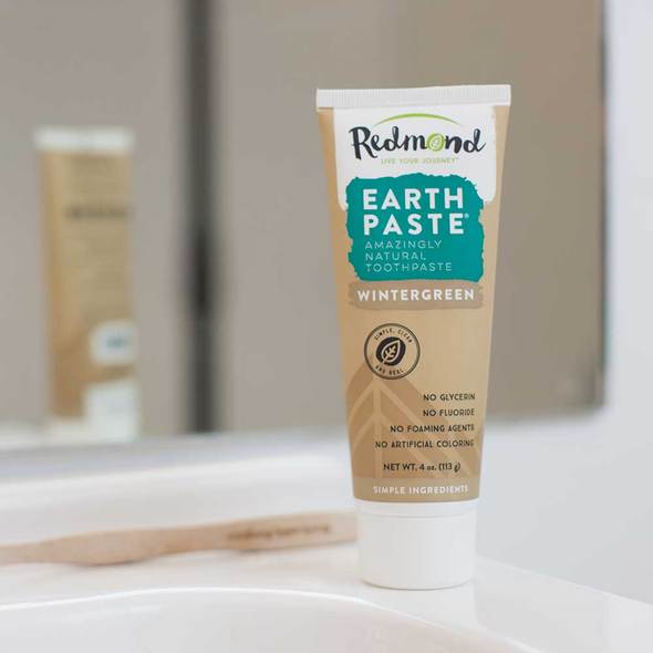 A brown tube of Redmond Wintergreen Earthpaste sits next to a toothbrush.