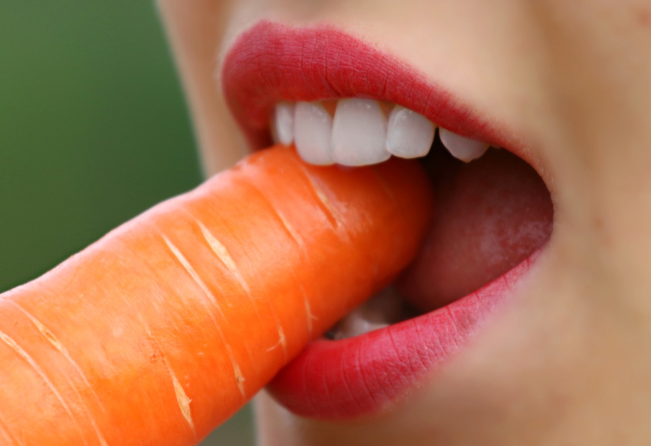 Girl showing her teeth as she bites into a carrot