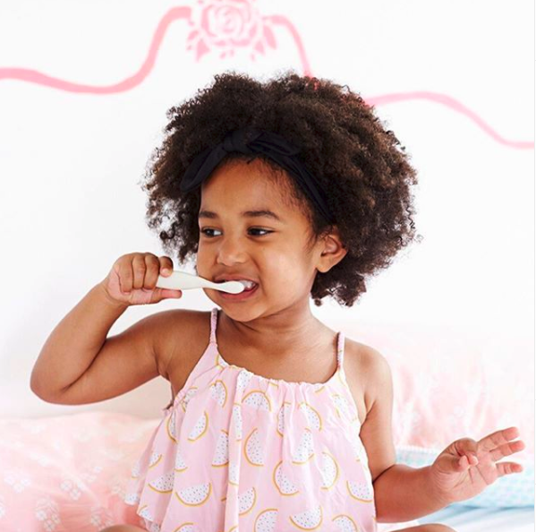 A little girl happily brushing her teeth with natural toothpaste.