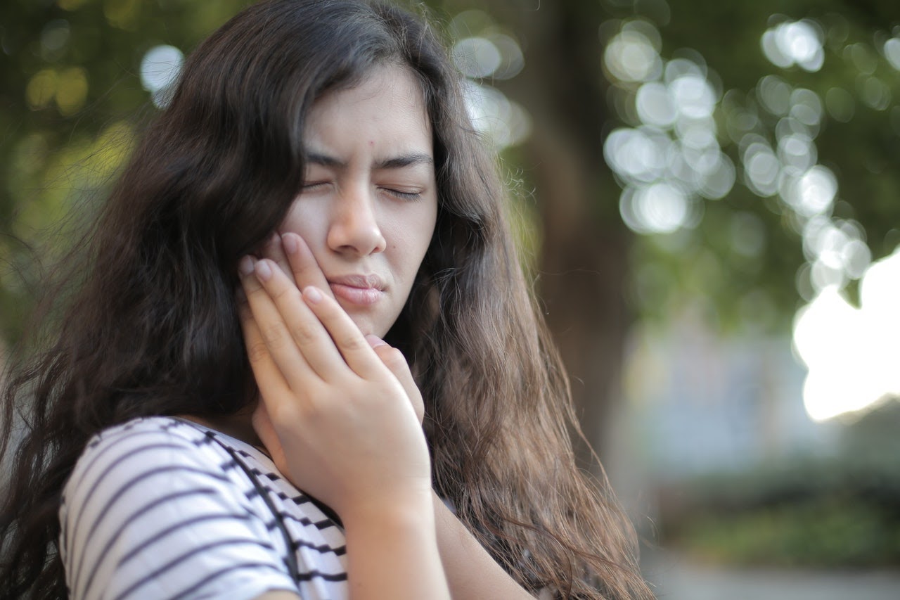 A woman clutches her face because of pain in her mouth.