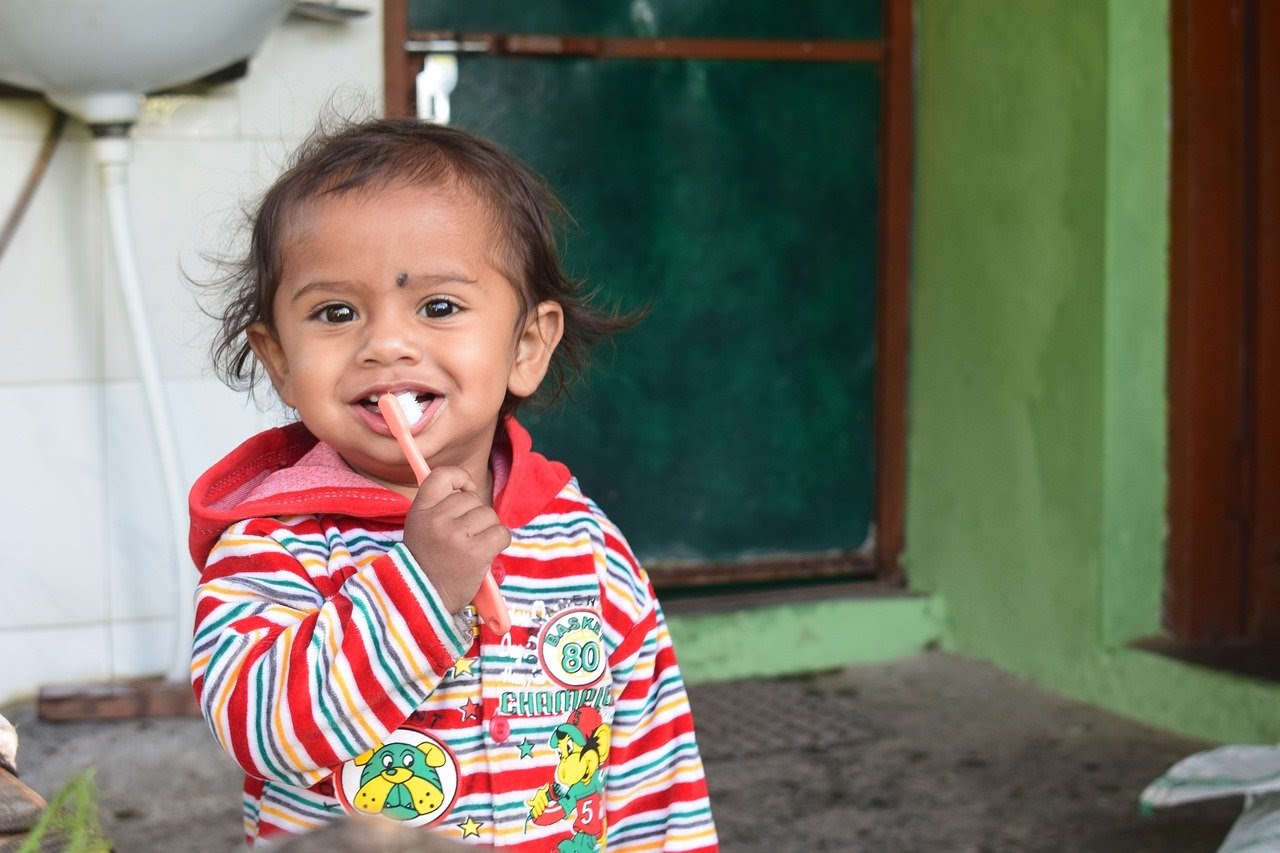 A small child brushes their teeth with an orange toothbrush.