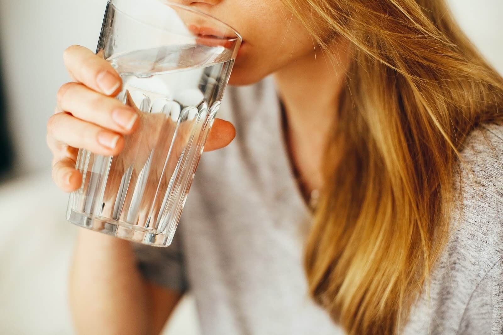 A blonde woman in a gray shirt drinking a glass of water.