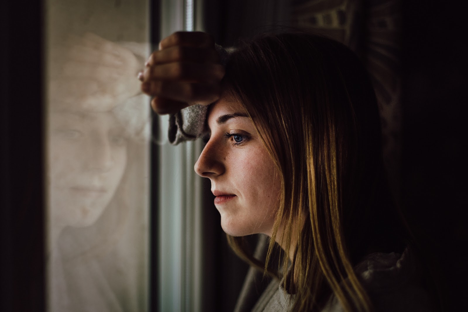 A blonde woman ponders while looking out her window.