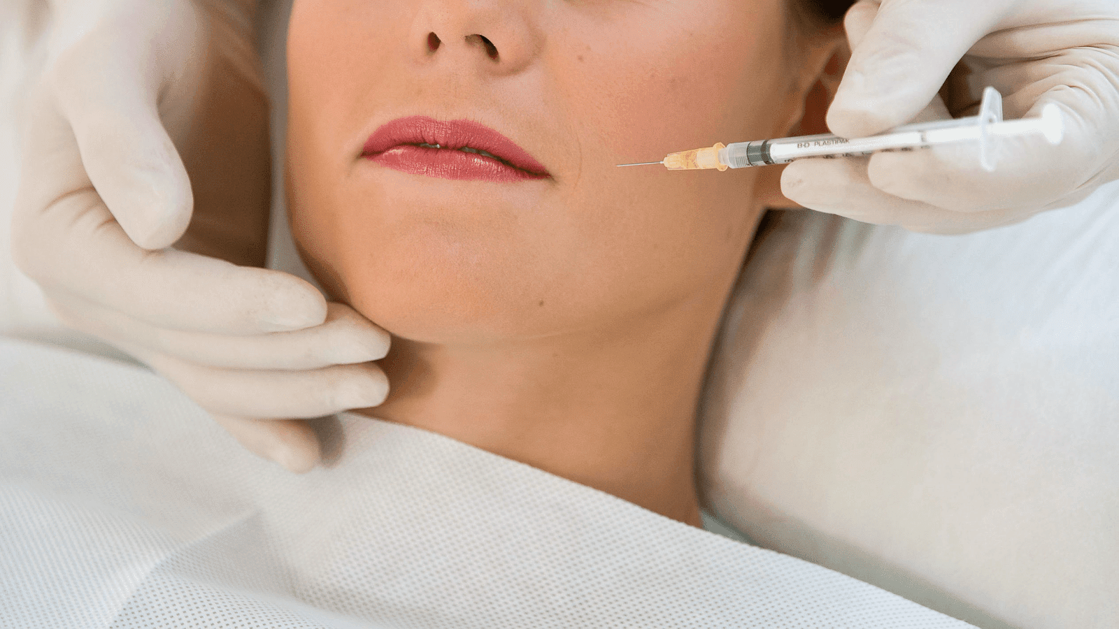 A woman with red lips gets a botox injection in her cheek.