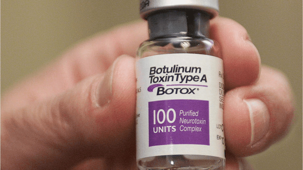 A hand holding a white and purple bottle of Botulinum Toxin.