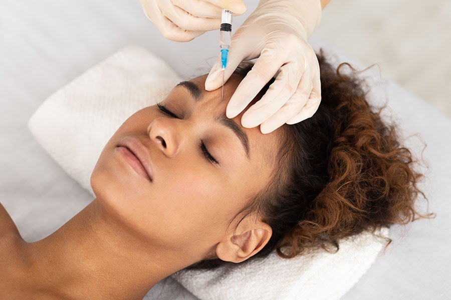 A young woman lays on a white towel and receives botox injections.