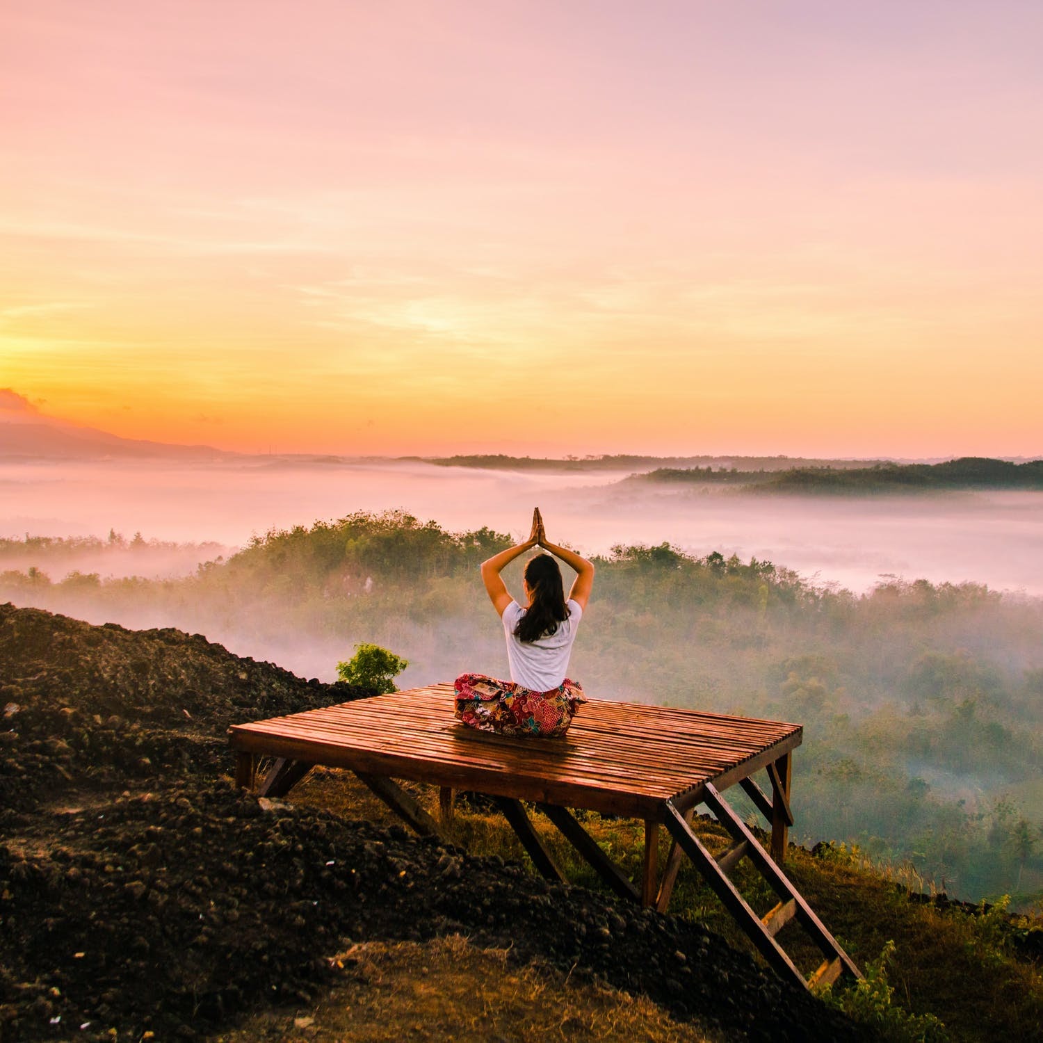 A woman practices yoga on a deck in front of a foggy landscape.