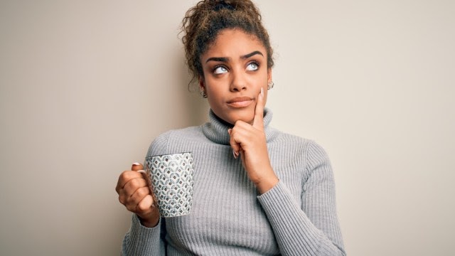 A woman in a gray turtleneck drinking coffee and thinking about sleep apnea.
