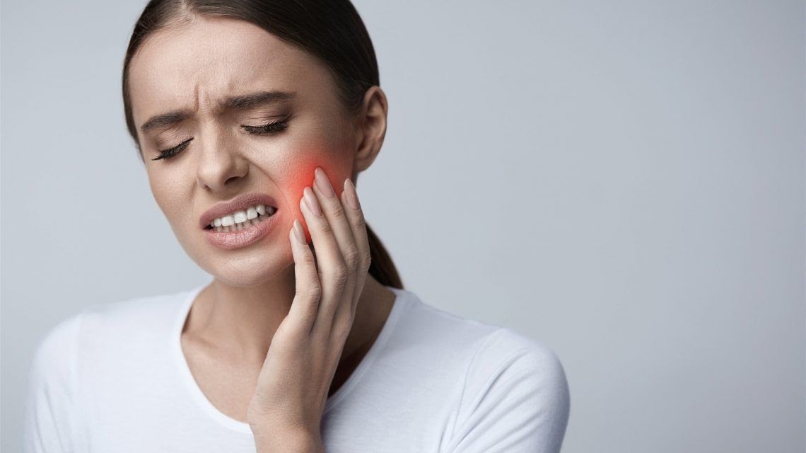 A woman presses on her cheek due to tooth pain.