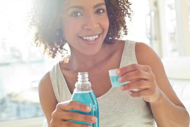 A woman in a gray tank top rinses with blue mouthwash.