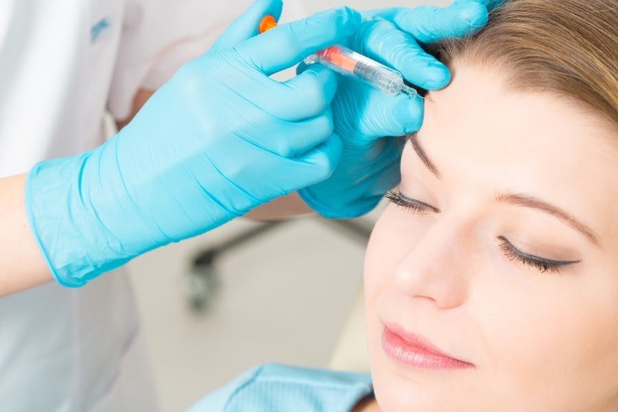 a woman receives Botox injections in her forehead from her doctor