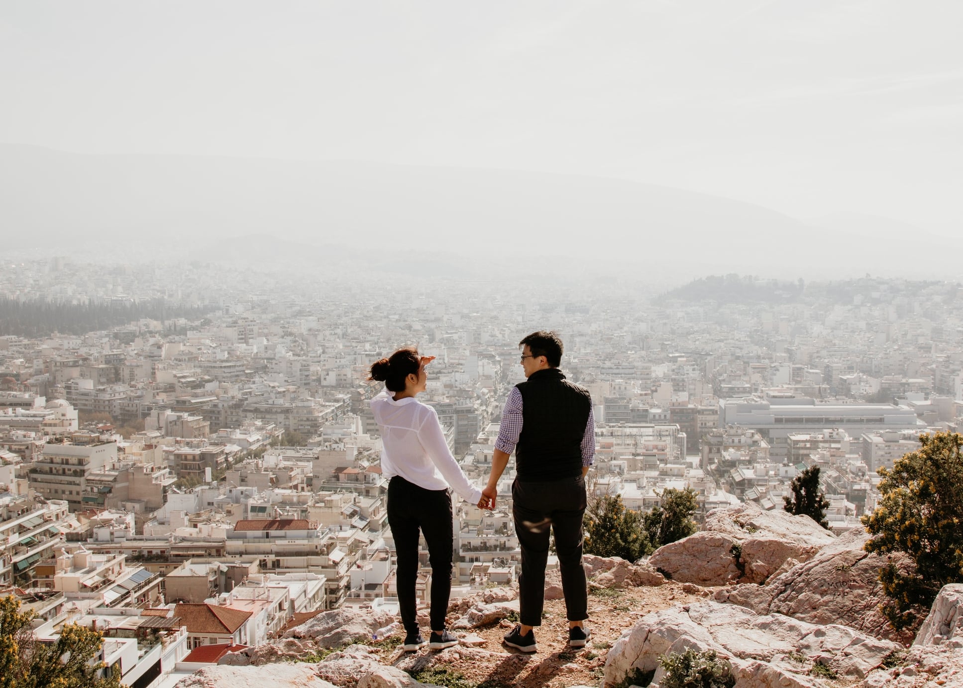 A couple, holding hands, overlooking a city from a look out point
