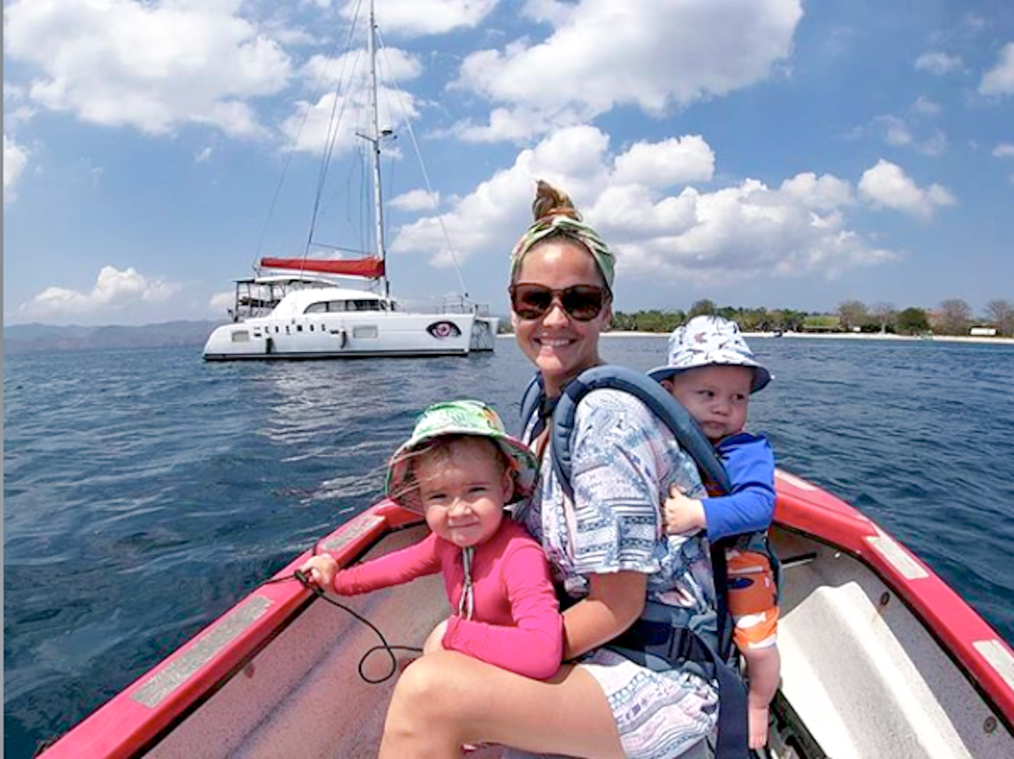 A happy family on a dingy boat, with their sailboat in the background